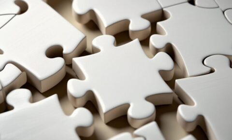 Nahaufnahme mehrerer weißer Puzzleteile, die ineinandergreifen – ein Puzzleteil liegt zentral im Fokus