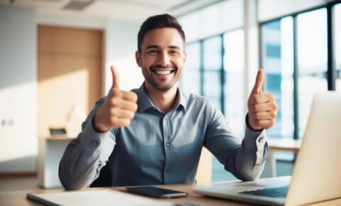 Zufriedener Mann im Büro zeigt Daumen hoch vor Laptop